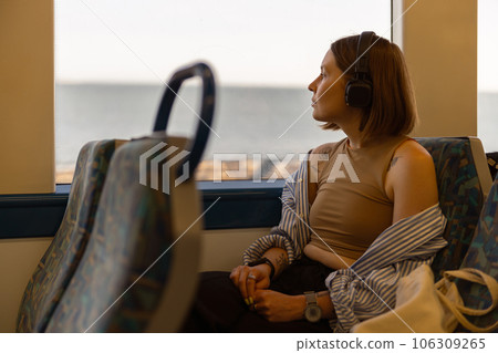 Woman in headphones while traveling in public transport and looking view outside the window 106309265