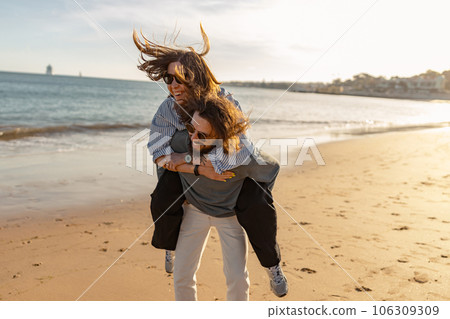 Handsome couple in love hugging while walking along the beach on sunny windy day 106309309
