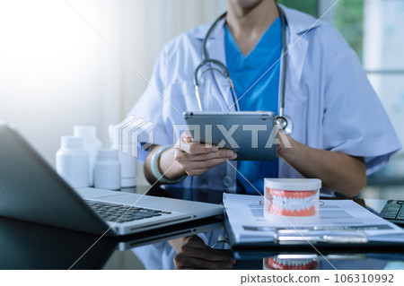 Dentist sitting at table with jaw samples tooth model and working with tablet and laptop in dental office professional dental clinic. medical doctor working.Dentist sitting at table with jaw samples Dentist sitting at table with jaw samples tooth model and working with tablet and laptop in dental office professional dental clinic. medical doctor working.Dentist sitting at table with jaw samples 106310992