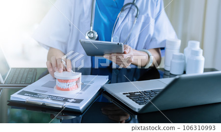 Dentist sitting at table with jaw samples tooth model and working with tablet and laptop in dental office professional dental clinic. medical doctor working.Dentist sitting at table with jaw samples 106310993