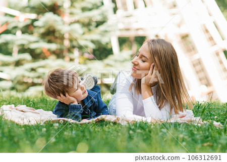 Beautiful cute young mom with her cute little son having fun lying on the grass in the park outdoors Beautiful cute young mom with her cute little son having fun lying on the grass in the park outdoors 106312691