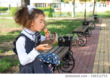 Girl with backpack eating sandwich packed in a sandwich box near school. A quick snack with a bun, unhealthy food, lunch from school. Back to school. Education, primary school classes, September 1 Girl with backpack eating sandwich packed in a sandwich box near school. A quick snack with a bun, unhealthy food, lunch from school. Back to school. Education, primary school classes, September 1 106312733