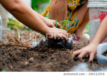 Little girl and mom grow plants in pots from recycled water bottles in the backyard. Recycle water bottle pot, gardening activities for children. Recycling of plastic waste 106312958