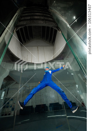 A man in overalls and a protective helmet enjoys flying in a wind tunnel. Free fall simulator 106313487