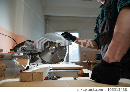 The master cuts the board with a circular saw in the workshop. Close-up of a carpenter's male hands at work. The master cuts the board with a circular saw in the workshop. Close-up of a carpenter's male hands at work. 106313488