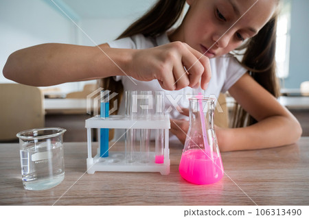 A schoolgirl conducts experiments in a chemistry lesson. Girl pouring colored liquids from a beaker. A schoolgirl conducts experiments in a chemistry lesson. Girl pouring colored liquids from a beaker. 106313490