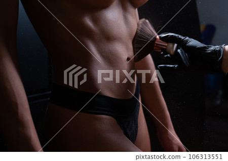 The master uses a brush to apply matting powder to a woman's flat stomach after an instant tanning procedure. The master uses a brush to apply matting powder to a woman's flat stomach after an instant tanning procedure. 106313551