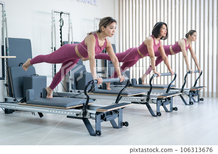 Three asian women doing plank with leg raised on reformer machine.  106313676