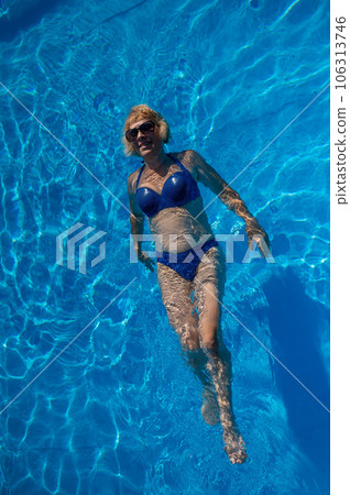 An elderly woman in sunglasses swims on her back in the pool. Vacation in retirement.  106313746