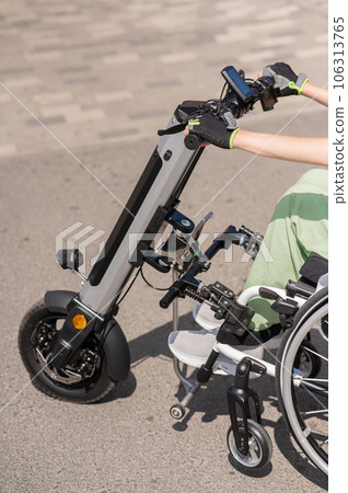 A woman controls a wheelchair using a special manual device. Close up an electric handbike. A woman controls a wheelchair using a special manual device. Close up an electric handbike. 106313765