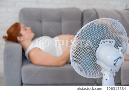 Pregnant woman suffers from heat and lies on the sofa near the electric fan.  106313884