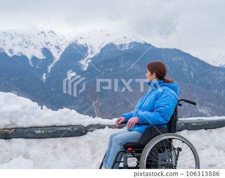 Caucasian woman in a wheelchair travels in the mountains in winter. 106313886