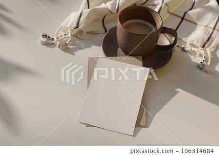 Cozy breakfast still life. Blank greeting card, invitation mockup in sunlight, shadows. Cup of coffee, white checkered plaid on table. Elegant winter, Christmas concept. Flatlay, top view. Copy space. 106314684