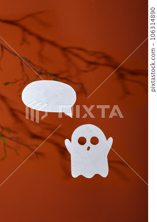 White paper ghost with a bubble for text on an orange background with shadows of tree branches 106314890