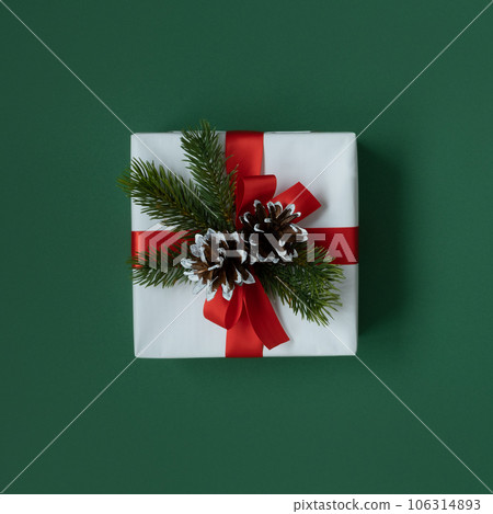 A white gift box with a red ribbon, cones and fir branches on a white background. Top view. 106314893