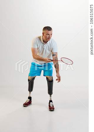 Full length of confident man with prosthesis play badminton indoors and enjoying his hobby against white studio background. 106315075