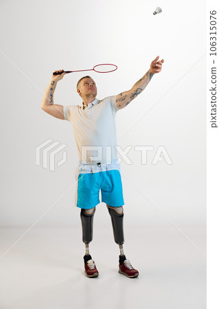 Full length of nice positive man with prosthesis play badminton indoors and enjoying his hobby against white studio background. 106315076