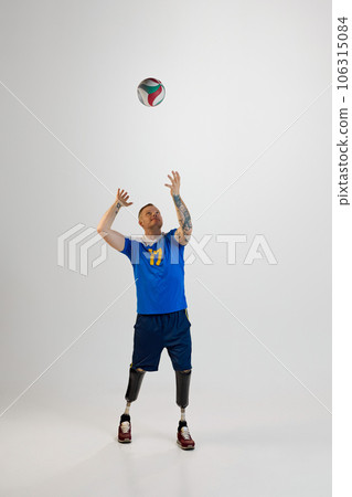 Attractive young man with prosthetic leg disability standing catching volleyball ball. Inclusive sport for people with disabilities. Attractive young man with prosthetic leg disability standing catching volleyball ball. Inclusive sport for people with disabilities. 106315084