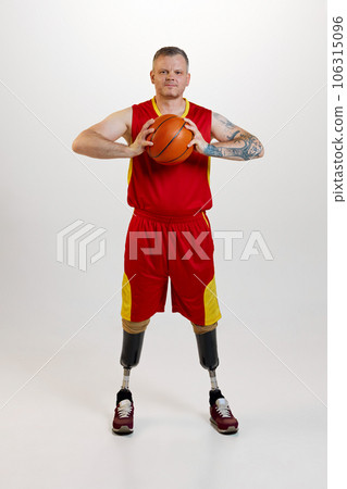 Attractive man with prosthetic leg disability standing holding orange basketball ball. Inclusive sport for people with disabilities. 106315096