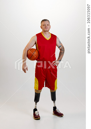 Attractive man amputee with prosthetic leg disability standing holding orange basketball ball. Inclusive sport for people with disabilities. 106315097