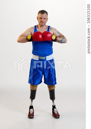 Full length of attractive positive man with prosthesis in boxing uniform training indoors and enjoying his hobby against white background. 106315100