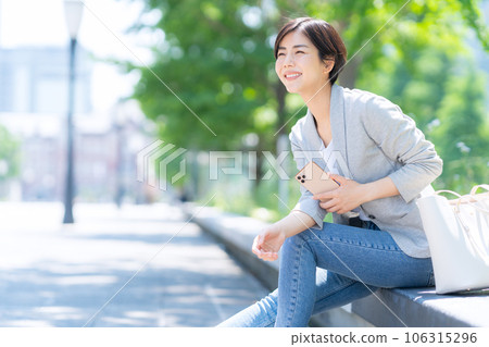 A young business woman in office casual clothes taking a break while looking at her smartphone in the office district 106315296