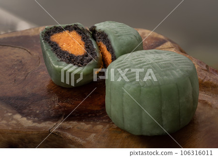Delicious green mooncakes is filled with taro, black sesame and golden thread egg on wooden cutting board. 106316011