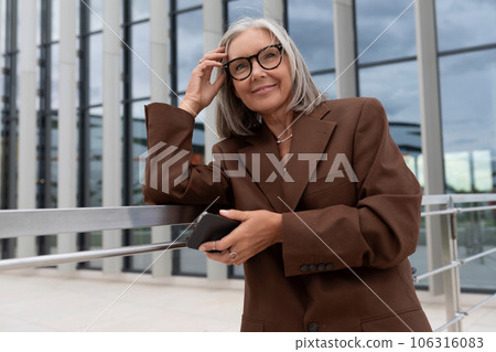 confident charming mature old lady with gray hair and glasses is dressed in a stylish jacket in an 106316083