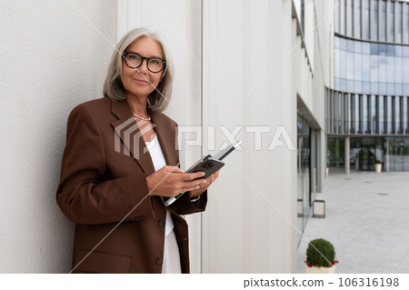 a slender gray-haired mature business lady dressed in a stylish jacket walks along the city streets 106316198
