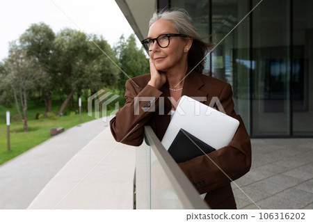 a slender gray-haired mature business lady dressed in a stylish jacket walks along the city streets 106316202