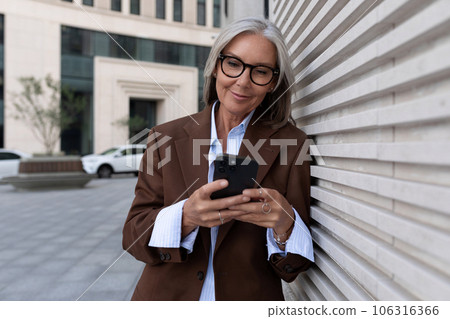 60 year old Caucasian business lady leader dressed in a brown stylish suit walks around the city 106316366