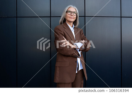 a successful business mature old woman with gray hair and glasses dressed in a stylish jacket walks 106316394