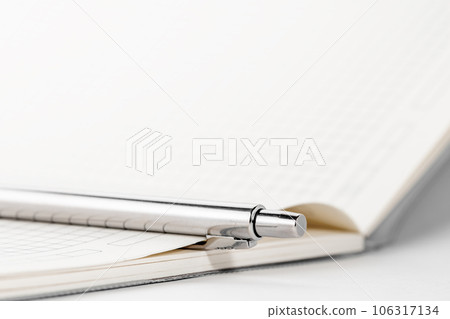White notebook with silver ballpoint pen. Empty white sheet on working table. Office stationery concept. White notebook with silver ballpoint pen. Empty white sheet on working table. Office stationery concept. 106317134