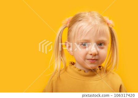 Round-faced portrait of little blonde girl with two tails. Girl with green eyes in yellow jacket, bright yellow background. Copy space Round-faced portrait of little blonde girl with two tails. Girl with green eyes in yellow jacket, bright yellow background. Copy space 106317420