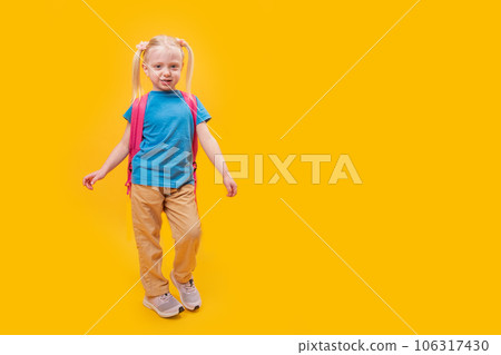 Full-length portrait of little caucasian girl with backpack on yellow background. Junior high school student with two ponytails. Copy space, mockup 106317430