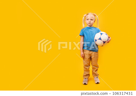 Full-length portrait of young girl with soccer ball. Yellow background. Girl loves football. Copy space, mockup 106317431