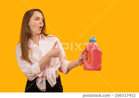Young woman holds pink plastic bottle container and shows thumbs up gesture like. Good detergent for washing or cleaning. Copy space, mock up. 106317452