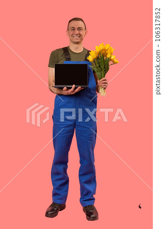 Full-length portrait of man in workers uniform holding laptop and bouquet of flowers isolated on pink background. Vertical frame. Copy space, mock up. Full-length portrait of man in workers uniform holding laptop and bouquet of flowers isolated on pink background. Vertical frame. Copy space, mock up. 106317852