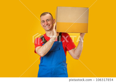 Courier dealer hold cardboard box isolated on yellow background. Smiling handsome caucasian delivery man with paper box. Copy space, mock up. Courier dealer hold cardboard box isolated on yellow background. Smiling handsome caucasian delivery man with paper box. Copy space, mock up. 106317854