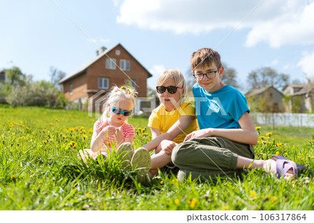 Happy childhood. Child siblings sits on dandelions filed on house background. Summer vacation time 106317864