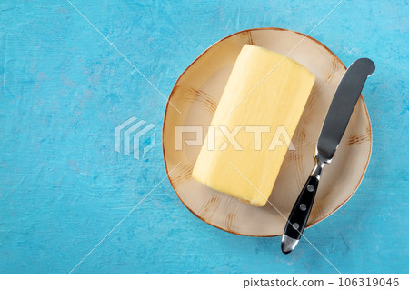 A stick of butter with a knife on a plate, top shot on a blue background A stick of butter with a knife on a plate, top shot on a blue background 106319046