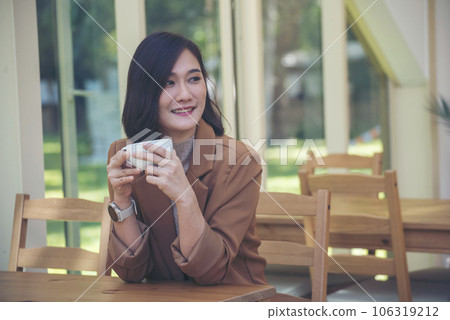 Asian Woman drink black coffee hand holding cup at green garden cafe. Young woman smile face love drink coffee. Beauty woman drinking black coffee in coffee shop holding freshness cup. Coffee lover Asian Woman drink black coffee hand holding cup at green garden cafe. Young woman smile face love drink coffee. Beauty woman drinking black coffee in coffee shop holding freshness cup. Coffee lover 106319212