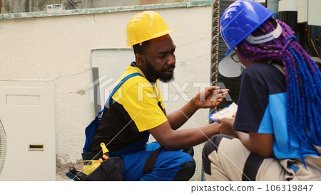 Precise serviceman reconditioning condenser using dusting brush to remove built up layer of dirt and dust that is slowing down internal components while coworker checks maintenance plan 106319847