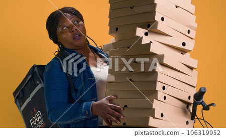 African american delivery person balancing plenty of pizza boxes for delivering to neighborhood. Active black woman on bicycle carefully carrying a big food order for transportation. African american delivery person balancing plenty of pizza boxes for delivering to neighborhood. Active black woman on bicycle carefully carrying a big food order for transportation. 106319952