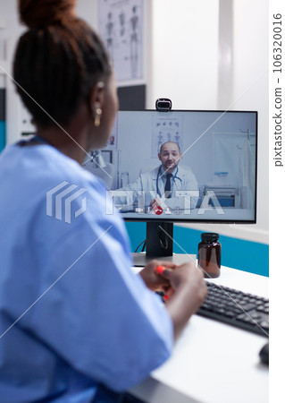 African american nurse at desk in a videocall communicating with doctor colleague in a professional medical office. Healthcare specialist doctor having online team meeting call with coworker 106320016
