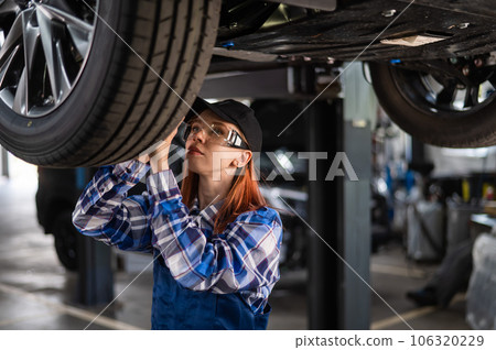 A female mechanic inspects a lifted car. A girl at a man's work. 106320229