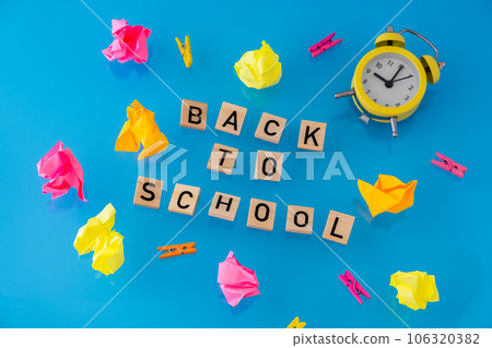 BACK TO SCHOOL message inscription text on wooden blocks on creative colorful blue background around stationery supplies and alarm clock. Levitating Educational greeting announcement for students and 106320382