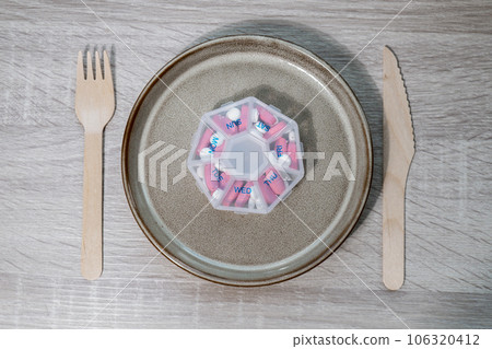 Organizer weekly shots with fork and knife medical pill box with doses of tablets for daily take medicine with white pink drugs and capsules. Daily vitamins at home. Health care and diseases cure Organizer weekly shots with fork and knife medical pill box with doses of tablets for daily take medicine with white pink drugs and capsules. Daily vitamins at home. Health care and diseases cure 106320412