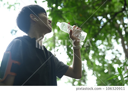 Happy asian male runner drinking water from a bottle, resting after trail running 106320911