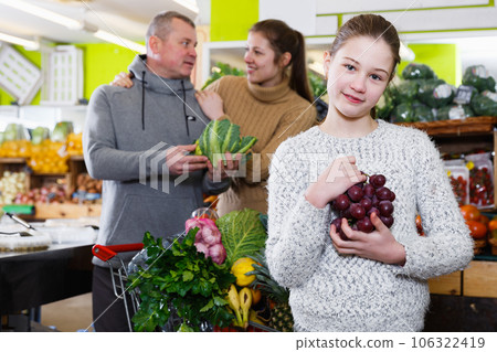 Girl holding grapes with family in fruit store 106322419